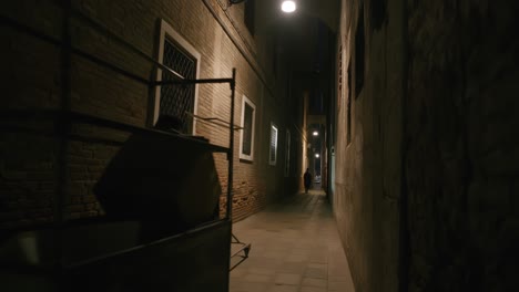 Venetian-alley-at-night:-A-dimly-lit-narrow-street-captures-pedestrians-passing-by-ancient-brick-walls