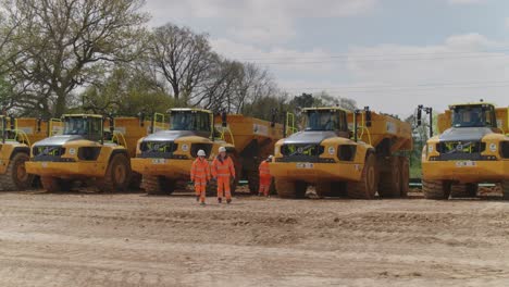 Construction-workers-in-high-vis-PPE-walk-amongst-a-fleet-of-construction-dump-trucks