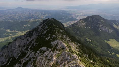 Impresionante-Vista-Aérea-De-Las-Montañas-Piatra-Craiului-En-Rumania,-Exuberantes-Valles-Debajo,-Bajo-La-Suave-Luz-Del-Día.