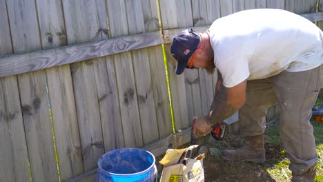 Man-drilling-hole-into-ground-for-fence-post,-medium-shot