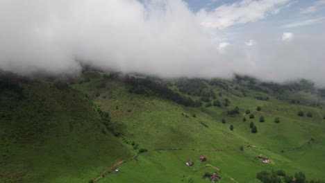 Ein-üppiges-Grünes-Tal-Mit-Tief-Hängenden-Wolken,-Bewaldeten-Hügeln-Und-Verstreuten-Ländlichen-Häusern,-Luftaufnahme