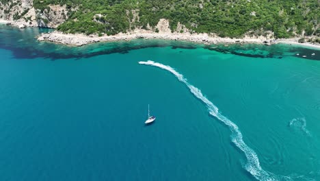 A-sailboat-on-the-vivid-blue-waters-near-corfu-island,-greece,-trails-in-the-sea,-aerial-view