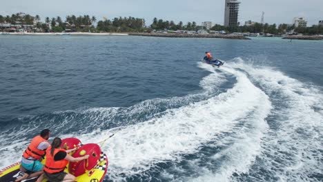 Couple-on-Beach-Vacation-Riding-Water-Tube,-Drone-Follow-Shot