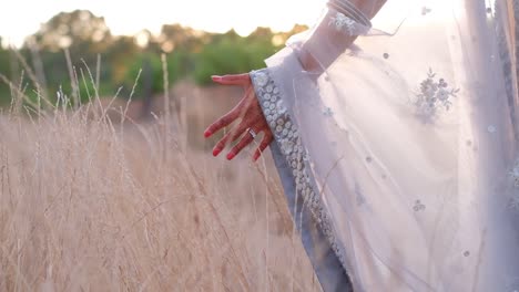 Vista-Recortada-De-Una-Novia-India-En-La-Naturaleza-Tocando-Campos-De-Hierba-Dorada-Al-Atardecer