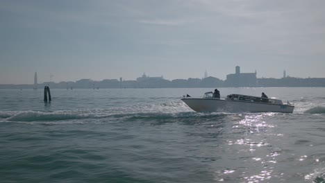Speedboat-gliding-across-Venice's-expansive-lagoon-with-city-skyline-backdrop,-Italy