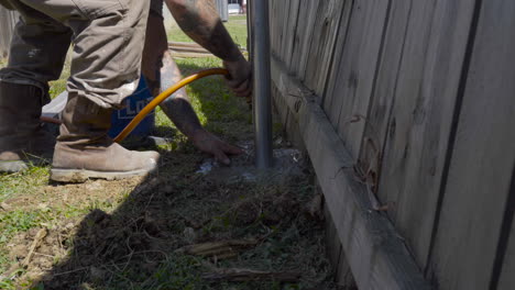 Hombre-Mezclando-Hormigón-Con-Agua-Alrededor-De-Un-Poste-De-Valla-Metálica