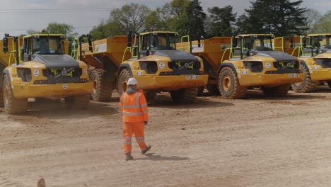 Un-Supervisor-De-Trabajadores-De-La-Construcción-Con-Ppe-Se-Acerca-A-Una-Flota-De-Camiones-Volquete-Listos-Para-Su-Inspección.