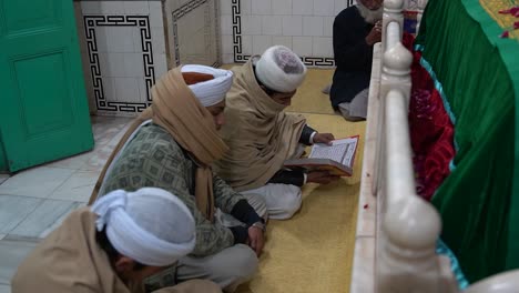 People-recite-the-Quran-at-a-shrine-built-over-a-grave,-engaging-in-a-cultural-practice-for-forgiveness