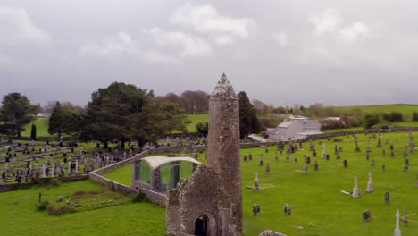 Dynamic-aerial-shot-of-Clonmacnoise,-highlighting-cemetery-and-round-tower