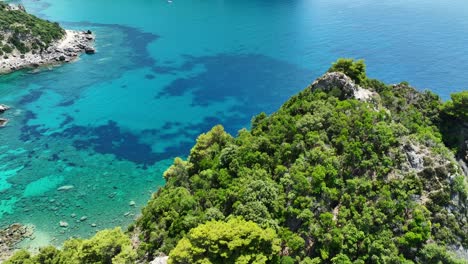 Lush-green-cliffs-on-corfu-island-with-crystal-blue-ionian-sea-waters,-aerial-view