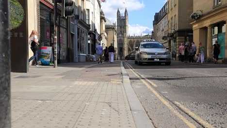 Street-in-Bath,-England-with-people-walking-on-the-sidewalks-and-cars-driving-in-slow-motion