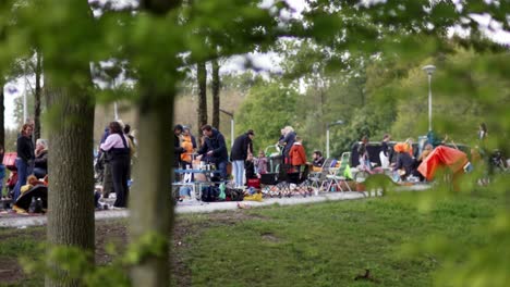 Child-running,-parents-behind-stills-on-Dutch-King'day-view-through-trees-in-Noorderpark