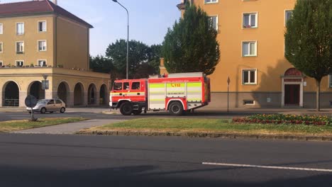 Camión-De-Bomberos-Tatra-815-Terrno-Cas-20-Que-Sale-De-Havirov,-República-Checa,-Frente-A-Casas-Construidas-En-Estilo-Arquitectónico-Sorela