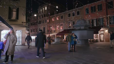 Festive-lights-illuminate-a-vibrant-Venetian-square,-casting-a-warm-glow-on-a-bustling-evening-scene
