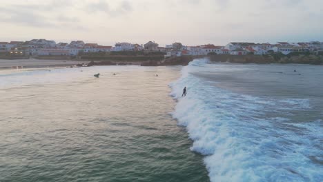 Toma-Aérea-De-Seguimiento-De-Un-Surfista-Surfeando-En-Una-Ola-Entre-Un-Grupo-De-Surfistas-En-El-Océano-Atlántico-Durante-La-Puesta-De-Sol-En-La-Playa-De-Baleal,-Portugal