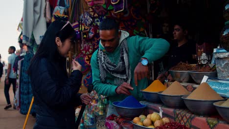 Local-craft-shop-owner-selling-goods-to-Asian-Tourist-in-market-street-of-Nubian-Village,-Aswan,-Egypt