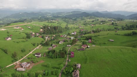 Lush-green-hills-of-Sirnea-village-with-scattered-houses-in-daylight,-aerial-view