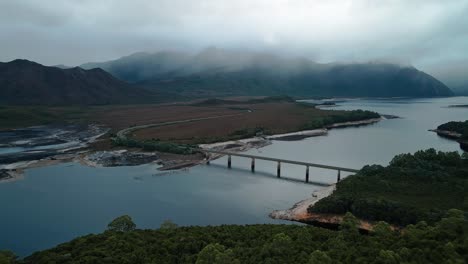 Aerial-drone-backward-moving-shot-over-Bradshaw-Bridge-that-spans-Lake-Burbury-on-western-coast-of-Tasmania,-Australia-surrounded-by-green-vegetation