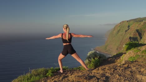 Frau-Lehnt-Sich-Während-Der-Goldenen-Stunde-In-Die-Krieger-Yoga-Pose-Auf-Einer-Klippe-Am-Meer