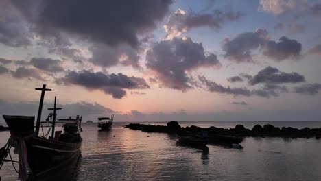 Twilight-hues-over-Koh-Samui's-tranquil-sea-with-boats-and-rocky-shore,-serene-mood