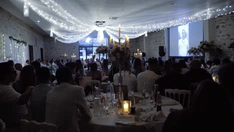 Slow-panning-shot-of-wedding-guests-sitting-at-their-table-watching-a-slideshow
