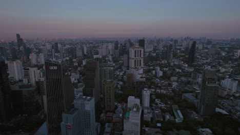 Aerial-drone-backward-moving-shot-over-office-buildings-and-residential-houses-in-Bangkok,-Thailand-after-sunset