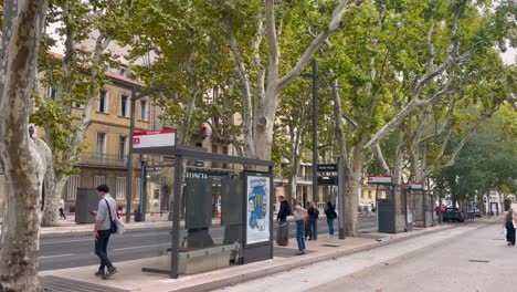 People-by-bus-stop-on-tree-lined-boulevard-in-Aix-en-Provence,-France