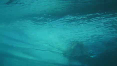 Blick-Von-Unter-Wasser-Auf-Die-Pulsierende-Wasseroberfläche,-Die-Wellen-Aufbaut,-Während-Der-Surfer-Die-Leine-Entlang-Reitet