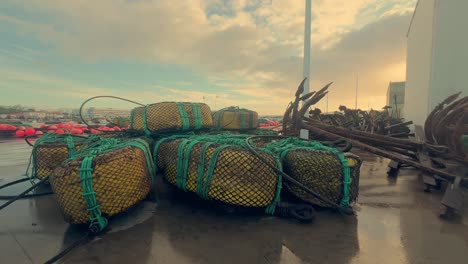 Fishing-gear-rests-on-the-moist-asphalt-in-a-coastal-town-of-Spain,-including-metal-anchors-and-nets,-representing-the-core-of-maritime-livelihood-and-coastal-heritage