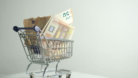 Shopping-cart-with-50-euro-paper-bill,-money-inside-flowing-business,-cash-studio-concept-shot
