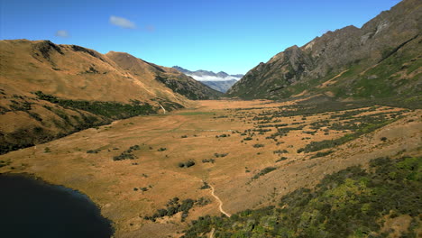 From-Moke-Lake-across-the-grasslands,-foothills-and-mountains-near-Queenstown,-New-Zealand---aerial-flyover
