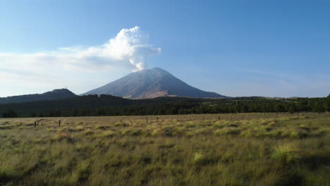 Aerial-view-low-over-alpine-meadow,-toward-the-active-Popocatepetl-volcano-in-Mexico