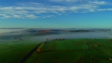 Tiefliegender-Nebel-über-Einer-Landschaft-Mit-Bauernhöfen-Und-Windturbinen---Pullback-Luftbild-Hyperlapse