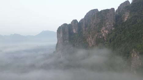 Drohnenschuss-Auf-Nebelverhangene-Klippen-In-Vang-Vieng,-Der-Abenteuerhauptstadt-Von-Laos