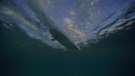 Rear-underwater-view-of-longboard-surfer-gliding-across-breaking-wave