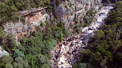 Aerial-drone-shot-over-narrow-river-gushing-through-the-rocks-at-Leven-Canyon-in-Tasmania,-Australia-on-a-sunny-day