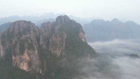 Drohnenaufnahme-Eines-Fluges-über-Klippen-Und-Nebliges-Tal-In-Vang-Vieng,-Der-Abenteuerhauptstadt-Von-Laos