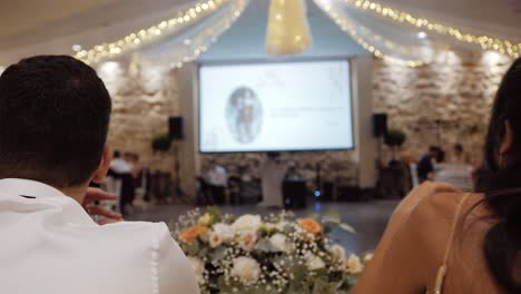 Slow-motion-shot-of-the-bride-and-groom-watching-a-slideshow-at-their-wedding