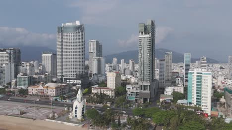 Eine-Filmische-Drohnenaufnahme,-Die-Den-Bezaubernden-Charme-Der-Skyline-Von-Nha-Trang-Einfängt,-Wo-Wolken-Träge-über-Der-Stadtlandschaft-Schweben,-Während-Der-Verkehr-Anmutig-Durch-Die-Belebten-Straßen-Fließt