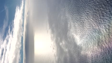 Aerial-view-of-blue-sky-and-sea,-clear-weather-bright-sun-water-ripples,-vertical