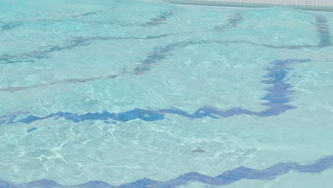 Waves-of-water-in-swimming-pool,-tile-pattern-on-bottom-refracted-through-water