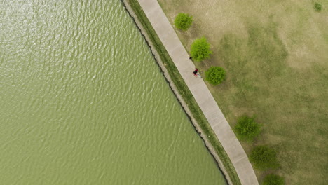 People-walking-by-a-lake-at-shelby-farms-park-in-memphis,-tennessee,-green-landscape,-daytime,-aerial-view