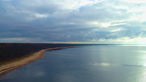 Coast-of-Baltic-Sea,-aerial-in-autumn-multicolor-tree-forest,-calm-water