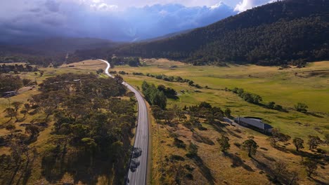 Beautiful-sunlight-on-rural-farm-house-and-country-road-with-dramatic-storm-clouds-above-Kosciuszko-National-Park,-NSW,-Australia