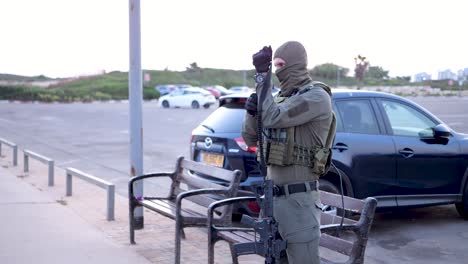 Armed-man-wearing-military-uniform-and-balaclava-picks-up-rifle-in-carpark