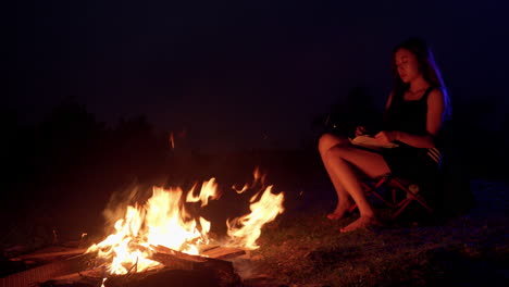 bonfire-camping-asiatic-young-female-model-sitting-in-front-of-fire-at-night-while-reading-a-book