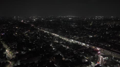 Aerial-drone-night-shot-of-metro-track-passing-through-traffic-on-the-highway