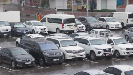 Öffentliche-Parkplätze-In-Der-Stadt,-Weiße-Autos,-Regnerischer-Tag,-Mann-Mit-Regenschirm,-Zeitlupe,-Dubai