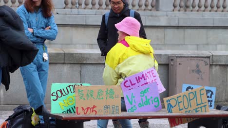 Protesters-at-Fridays-for-Future-school-strike-with-self-made-signs-on-bench-chatting,-close-static