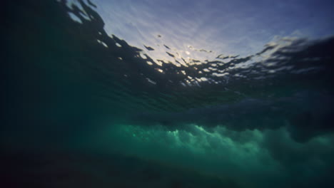 Sun-rays-glisten-below-breaking-ocean-wave-on-sand-bar,-cloud-texture